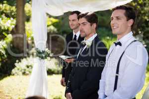 Groom standing with waiter and groomsman in park