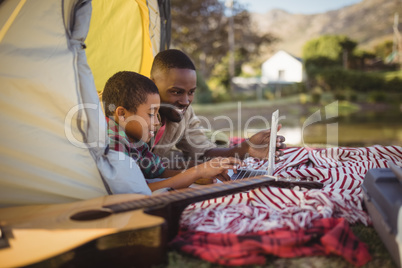 Smiling father and son using laptop in tent