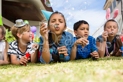 Children blowing bubbles while lying on field