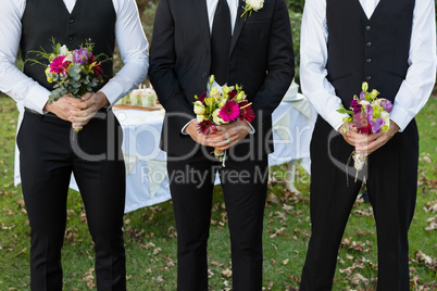 Bridegroom and best man standing with bouquet of flowers in garden