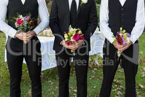 Bridegroom and best man standing with bouquet of flowers in garden