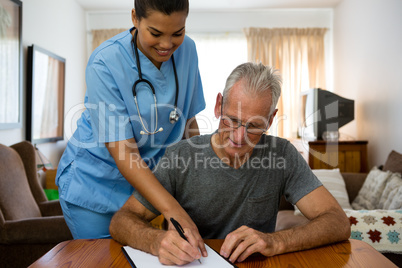 Doctor assisting senior man in writing at nursing home