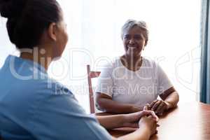 Side view of nurse interacting with senior woman at table