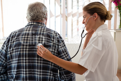 Female doctor examining senior patient with stethoscope at nursing home