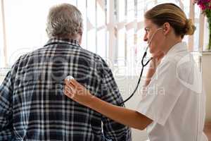 Female doctor examining senior patient with stethoscope at nursing home