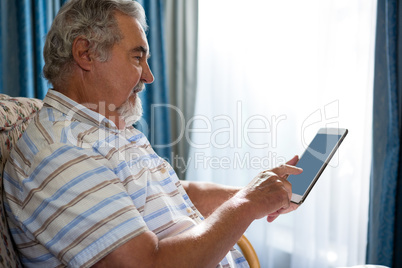 Side view of senior man using digital tablet while sitting on sofa