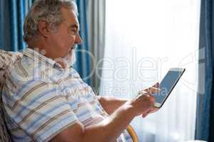 Side view of senior man using digital tablet while sitting on sofa