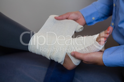 Physiotherapist putting bandage on injured feet of patient