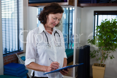 Portrait of smiling physiotherapist writing on clipboard