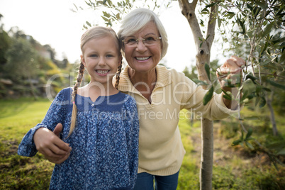 Smiling granddaughter and grandmother standing together in garden