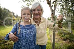 Smiling granddaughter and grandmother standing together in garden