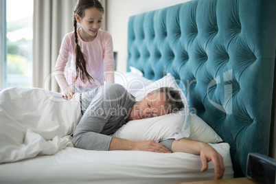 Girl waking her sleeping father up in bed