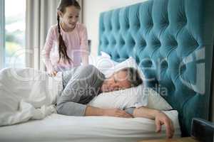 Girl waking her sleeping father up in bed