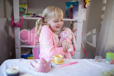 Smiling girl playing with a teddy bear and toy kitchen set