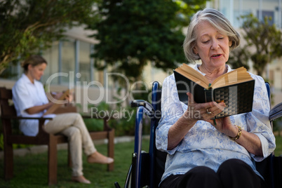 Senior woman reading book while doctor sitting in background