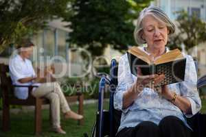 Senior woman reading book while doctor sitting in background