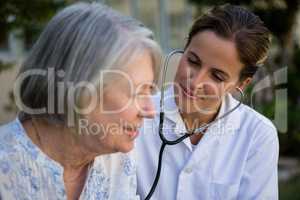 Female doctor examining senior woman with stethoscope