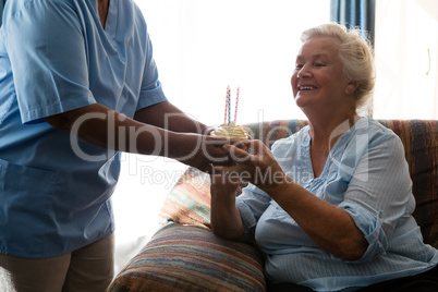 Happy senior woman looking at cup cake with candle held by nurse
