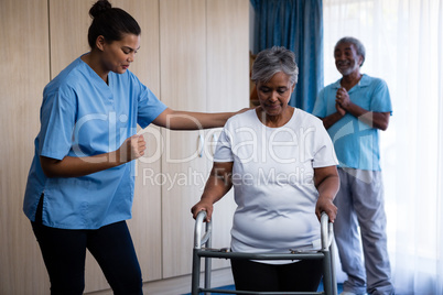 Nurse assisting senior woman in walking with walker