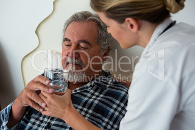 Side view of female doctor giving water to senior patient