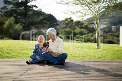 Granddaughter and grandmother sitting on the deck with digital tablet