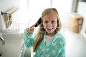 Smiling girl combing her hair in bathroom