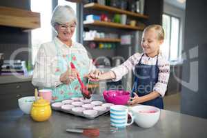 Smiling grandmother helping granddaughter while pouring cupcake batter