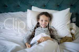 Smiling girl lying on bed with teddy bear in bedroom