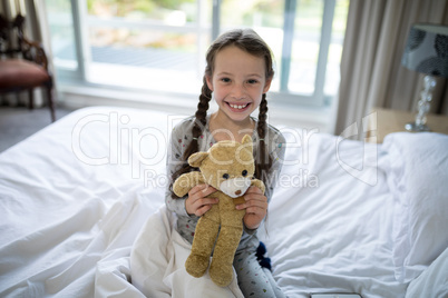 Girl holding teddy bear on bed in bedroom