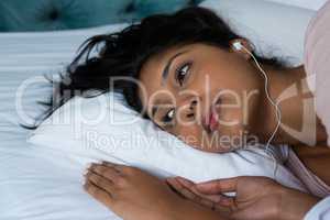 Thoughtful woman listening to music on bed