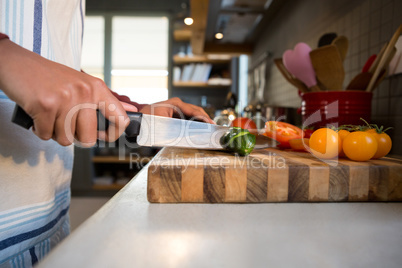 Mid section of woman cutting zucchini in kitchen