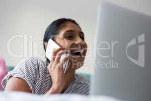 Happy woman with laptop talking on phone in bedroom