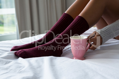 Low section of woman holding coffee cup on bed