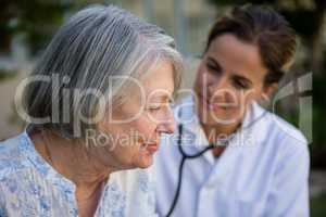 Female doctor examining senior woman with stethoscope in park