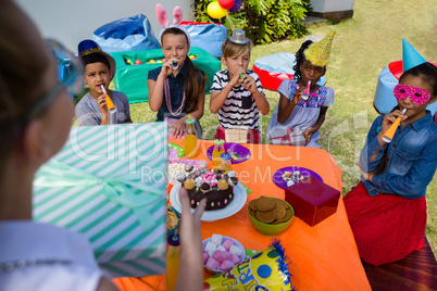 Girl holding gift while friends blowing party horn