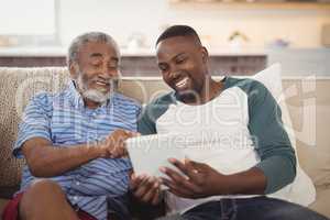 Smiling father and son using digital tablet in living room