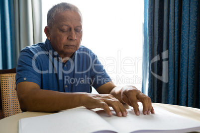 Senior man reading braille book in retirement home