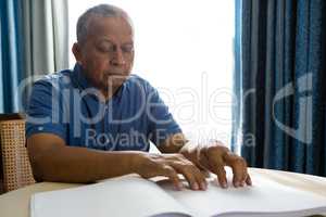 Senior man reading braille book in retirement home