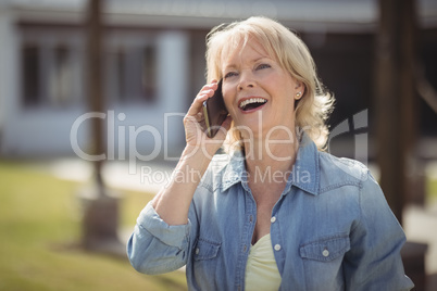 Senior woman talking on mobile phone outside his house