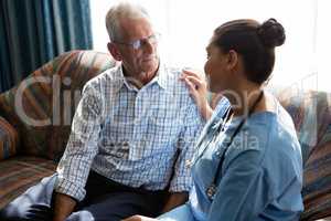 Female doctor consoling senior man on sofa in nursing home