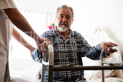 Female doctor standing by senior man holding walker in nursing home