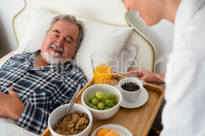 Cropped hand of female doctor serving food to senior patient relaxing on bed