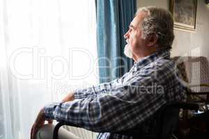 Senior man looking through window while sitting on wheelchair in retirement home