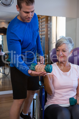 Male physiotherapist helping patient in performing exercise with dumbbell
