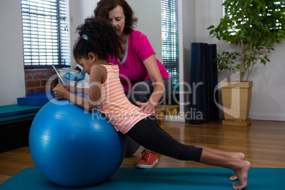 Female physiotherapist helping girl patient in performing stretching  exercise on exercise mat