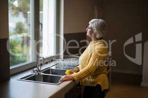 Senior woman standing near the kitchen sink and looking through window