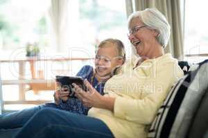 Smiling granddaughter and grandmother using digital tablet on sofa