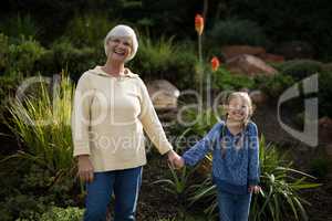 Smiling granddaughter and grandmother standing in garden