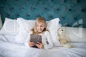 Girl using digital tablet while lying on bed