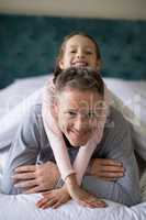 Smiling daughter lying on fathers back in bedroom